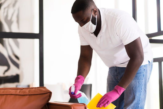 Man sanitizing surfaces with Hall's Retail hand sanitizer while wearing a mask and gloves.